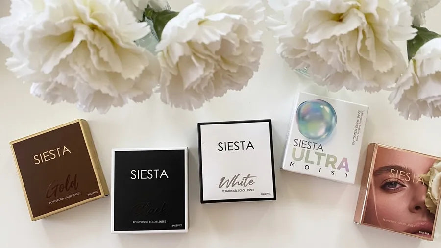 Caixas das lentes Siesta Gold, Black, White e Ultra Moist, com flores brancas